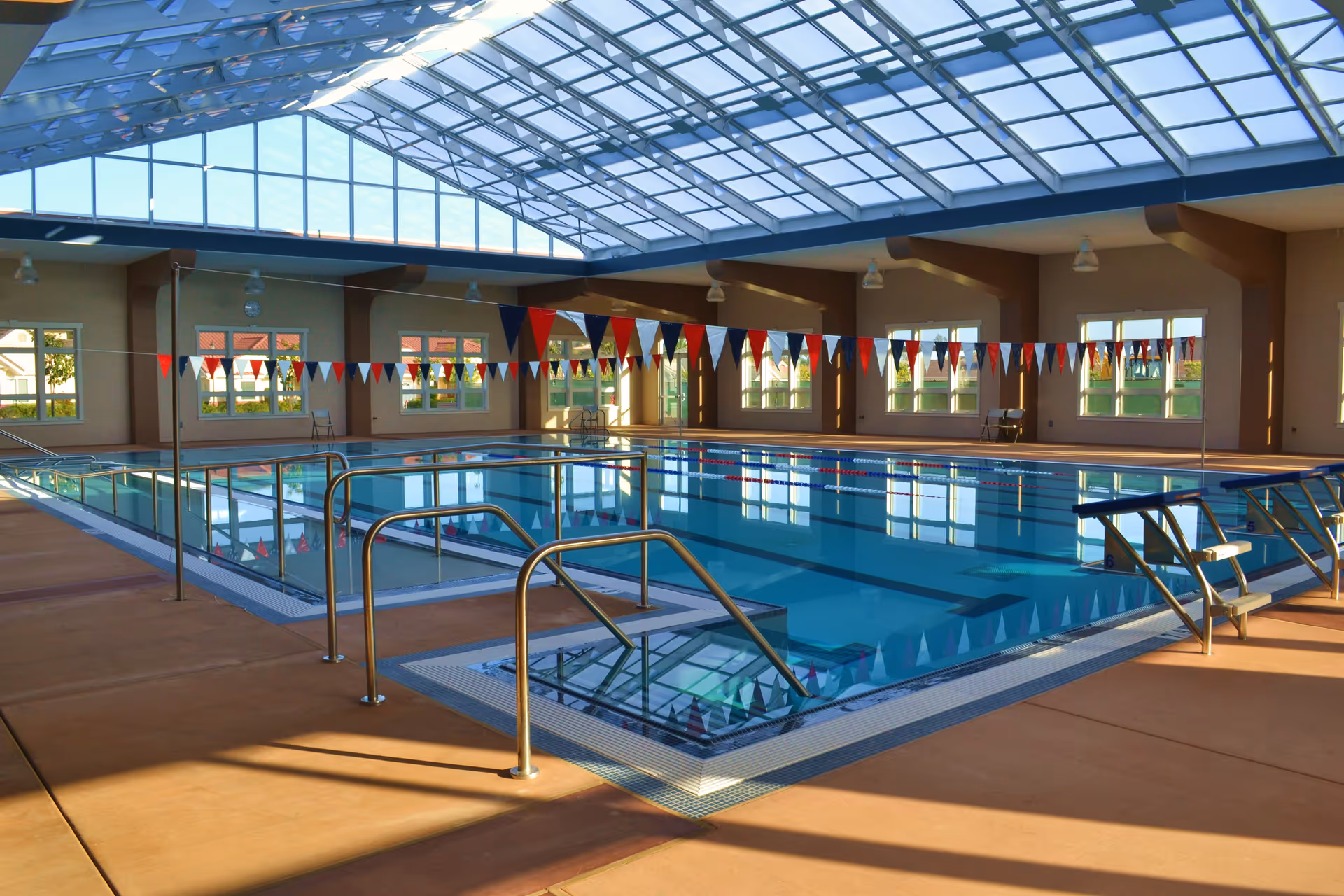 Bright indoor swimming pool with lane markers, skylight ceiling, and seating around the deck.
