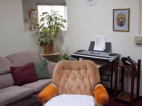 Cozy living room with sofa, chair, plants, and an electronic keyboard.