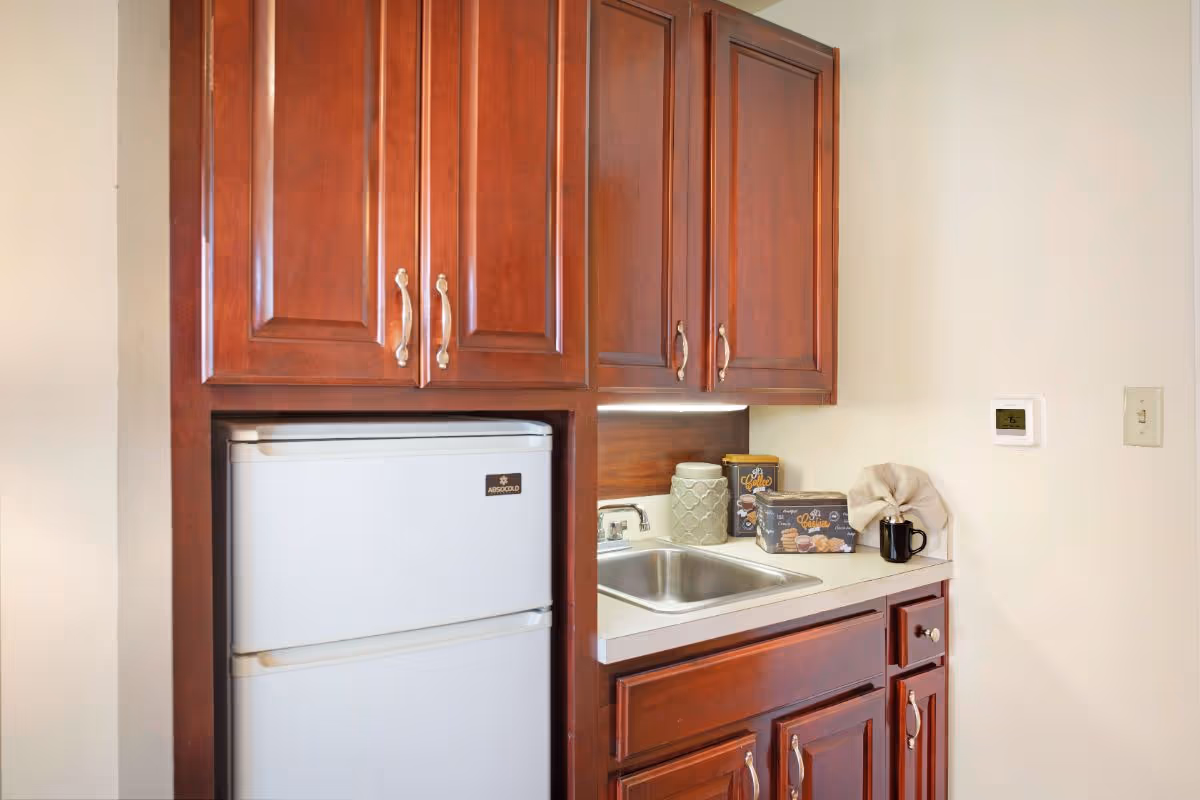 Small kitchenette featuring cherry wood cabinets, a compact refrigerator, a sink, and countertop containers and a mug.