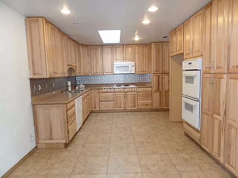 Large kitchen with light wood cabinetry, tiled floor, built-in double oven, microwave, dishwasher, and a skylight.