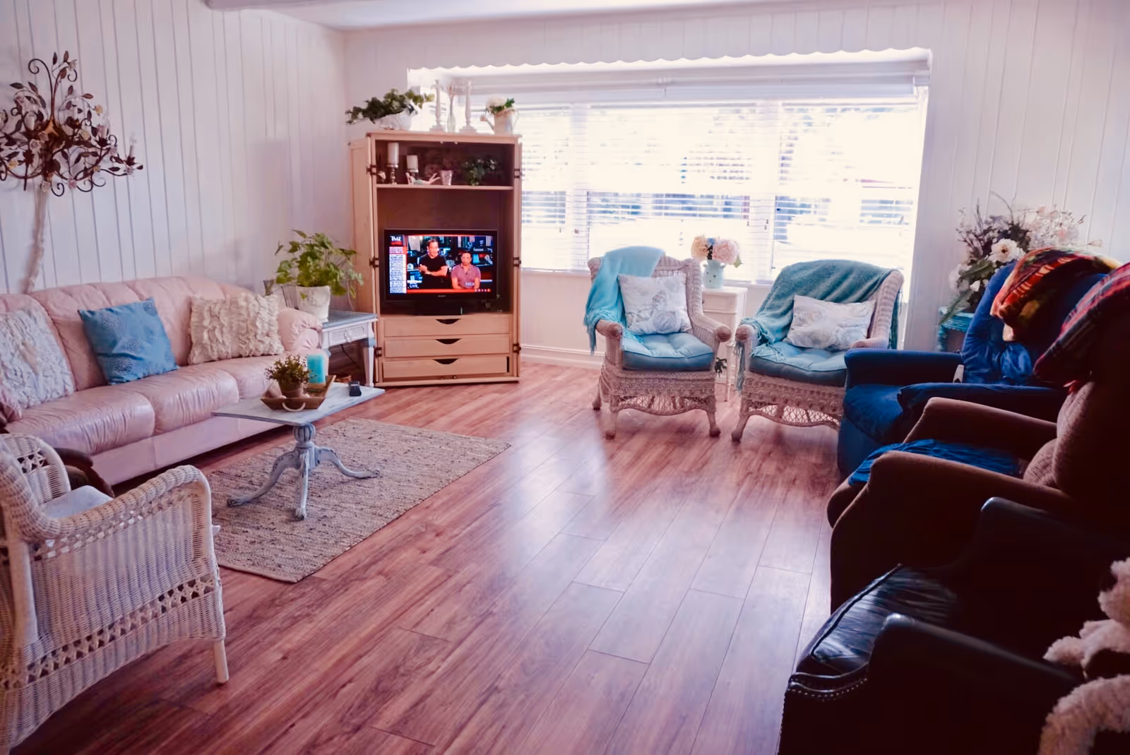 Bright, cozy communal living room with sofas, wicker chairs, a TV cabinet, and a large window letting in natural light.