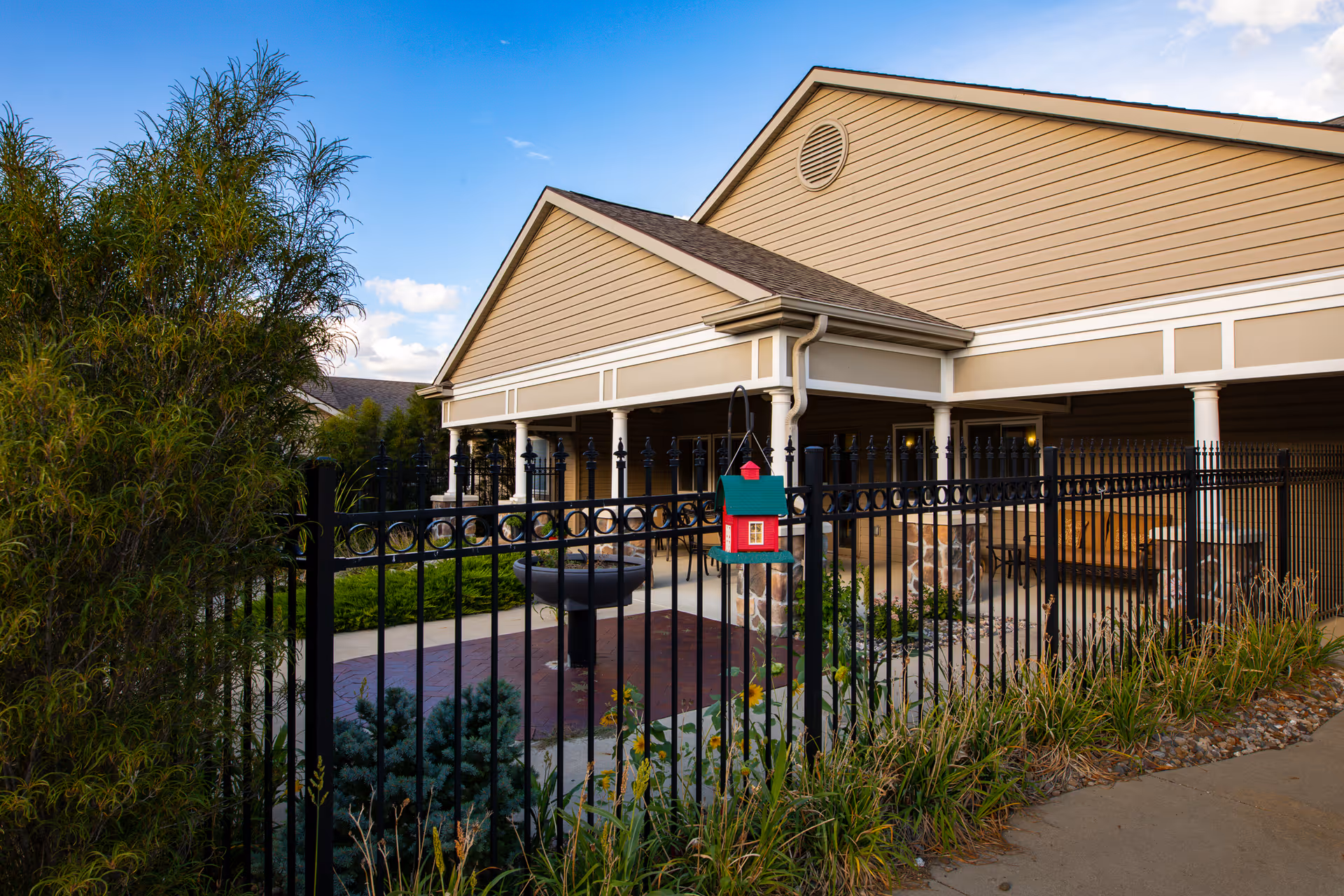 Exterior view of Homestead Assisted Living building entrance with a fenced courtyard, decorative birdhouse, and covered porch.