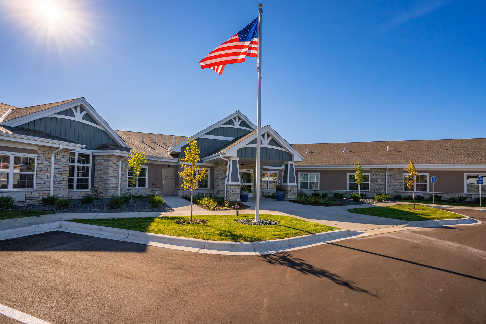 American flag on a tall pole stands before a modern senior living facility entrance.