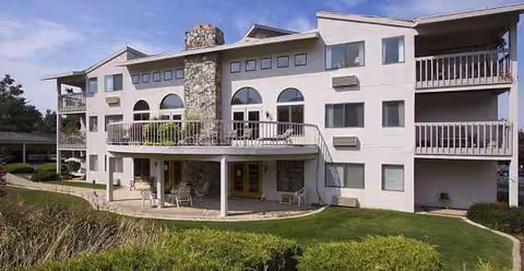 Exterior view of a multi-story retirement community with balconies and a manicured lawn.