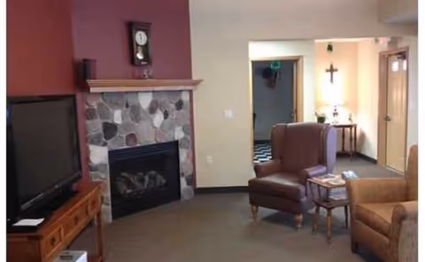 Cozy living room with stone fireplace, TV, armchairs, and hallway leading to other rooms.