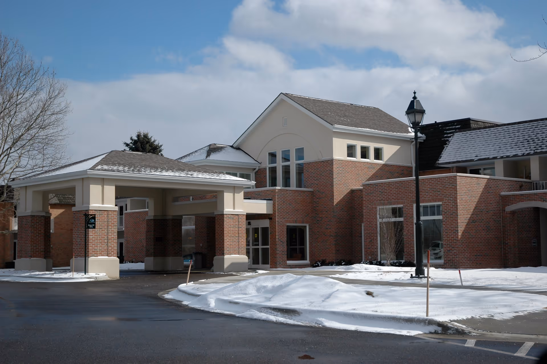 Exterior view of Porter Hills Village building with brick walls and beige accents, a covered entrance, snow on the ground, and a streetlamp in front under a partly cloudy sky.