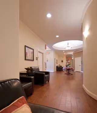 Long interior corridor of a memory care community with wood floors, seating along the wall, and a circular skylight.