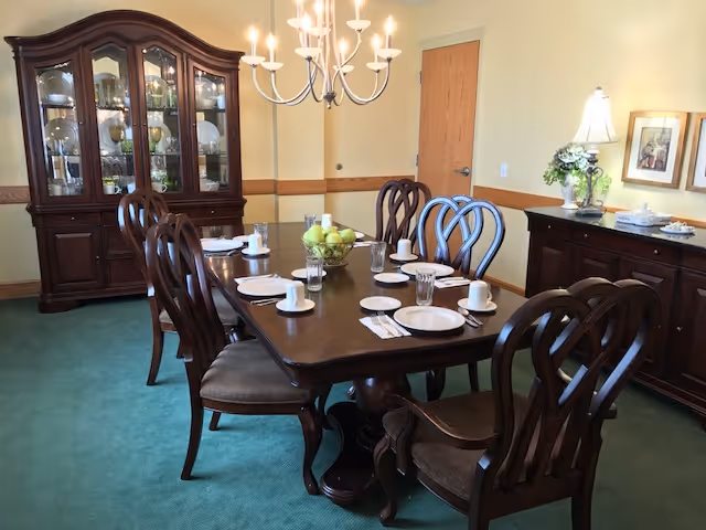 Formal dining room with a dark wooden table set for eight, matching chairs, a china cabinet, sideboard and chandelier.