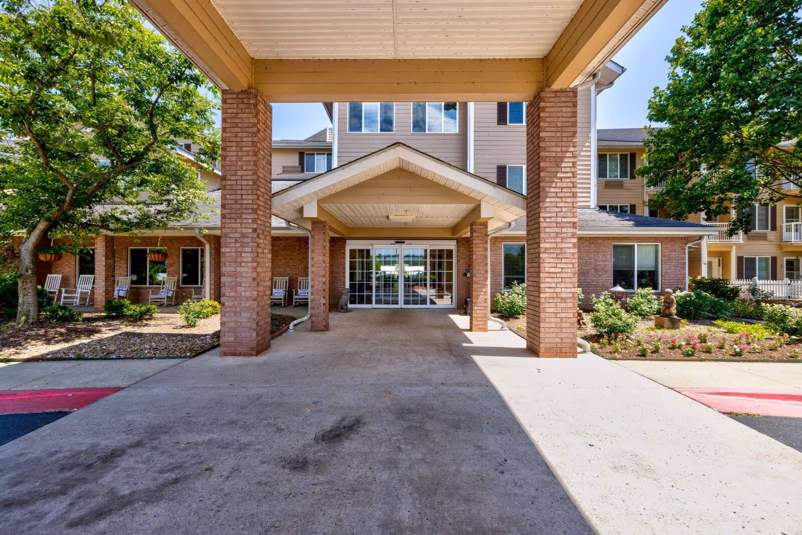 Covered driveway and main entrance of Morada Fort Smith with brick columns, rocking chairs, and landscaped beds.