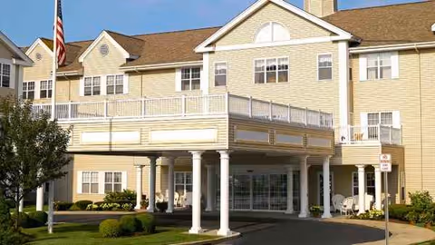 Exterior view of a beige senior living building with a covered entrance and white columns.