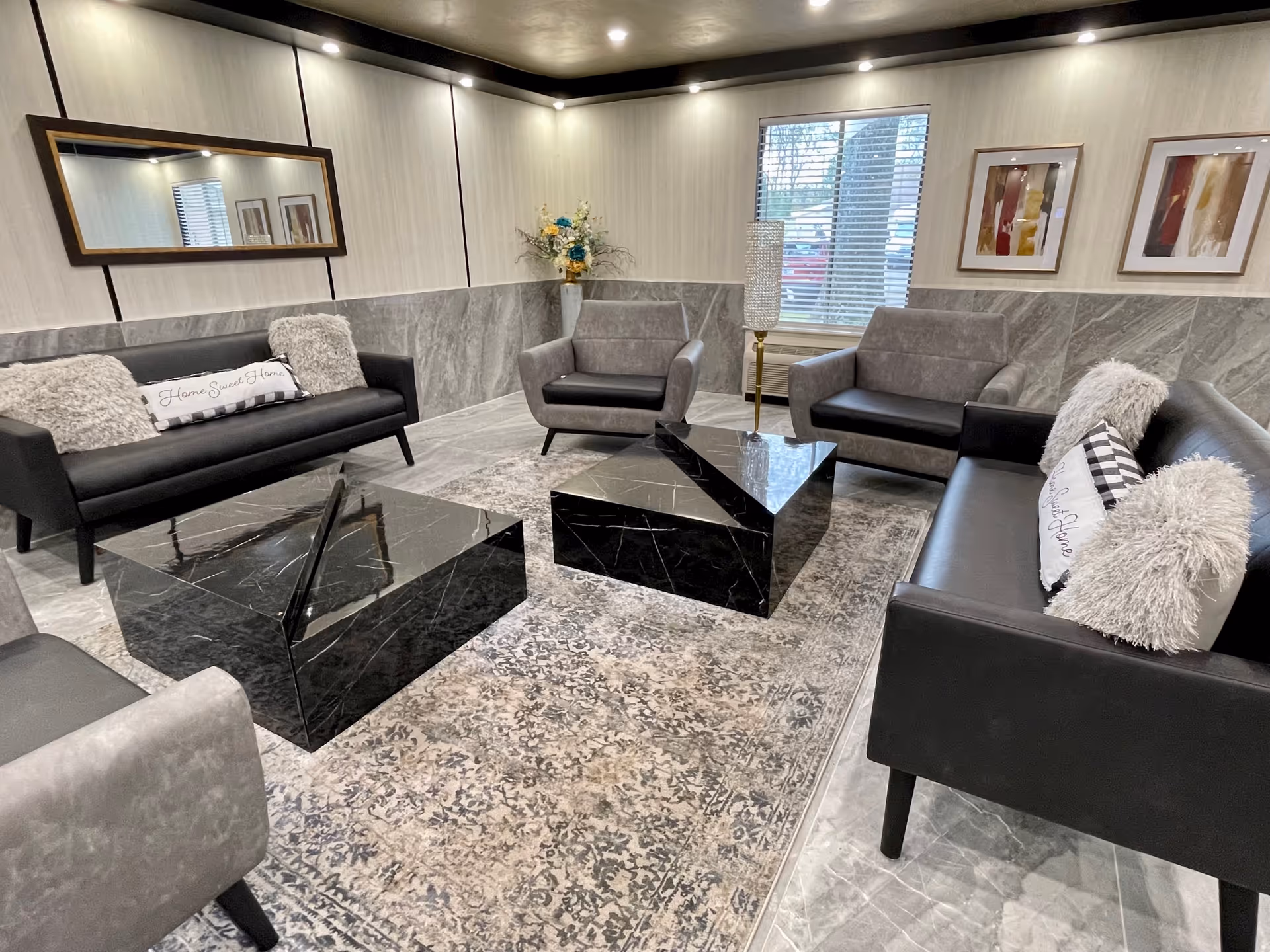A modern lounge with gray sofas and armchairs arranged around two black marble coffee tables on a patterned rug.