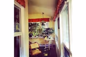 Enclosed sunroom with windows along one side, a small table, chairs, and potted plants.