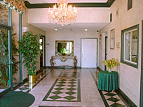 Lobby with patterned tile floor, chandelier, ornate console table beneath a mirror, and potted plants.
