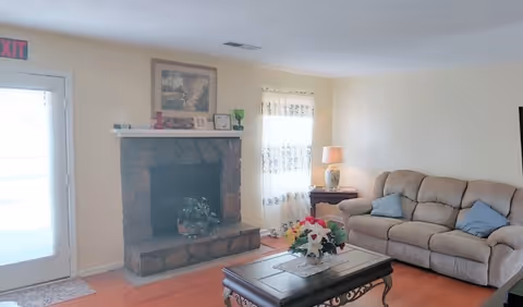 Cozy living room featuring a stone fireplace, beige sofa, coffee table, and flowers.