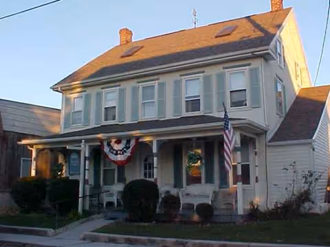 Front view of Charlotte's Home Inc, a two-story senior living house with porch, bunting, and flag.