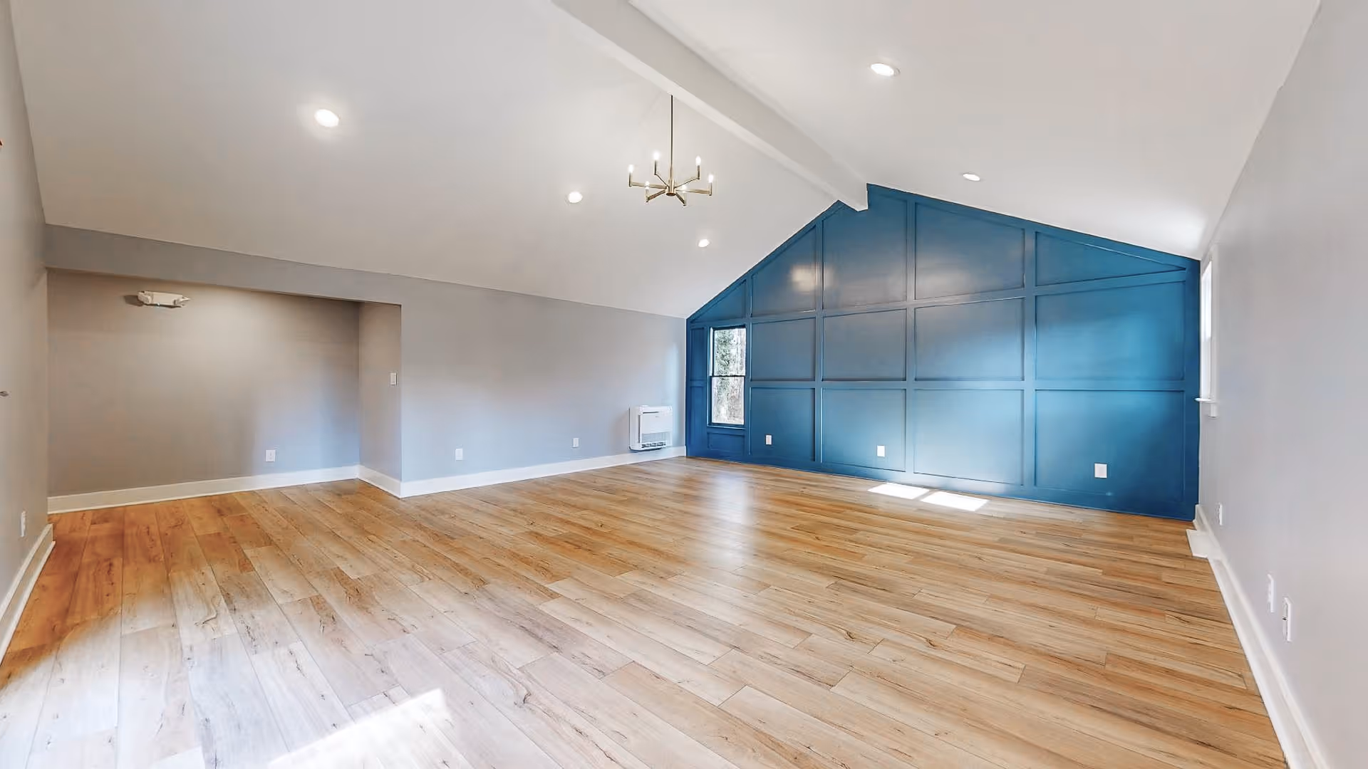 Spacious empty living room with vaulted ceiling, wood flooring, recessed lights and a blue paneled accent wall.