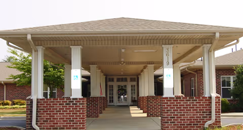 Covered entrance to a brick building with white columns and a peaked roof, featuring a walkway leading to glass double doors. The building has handicap accessible signs on the columns.