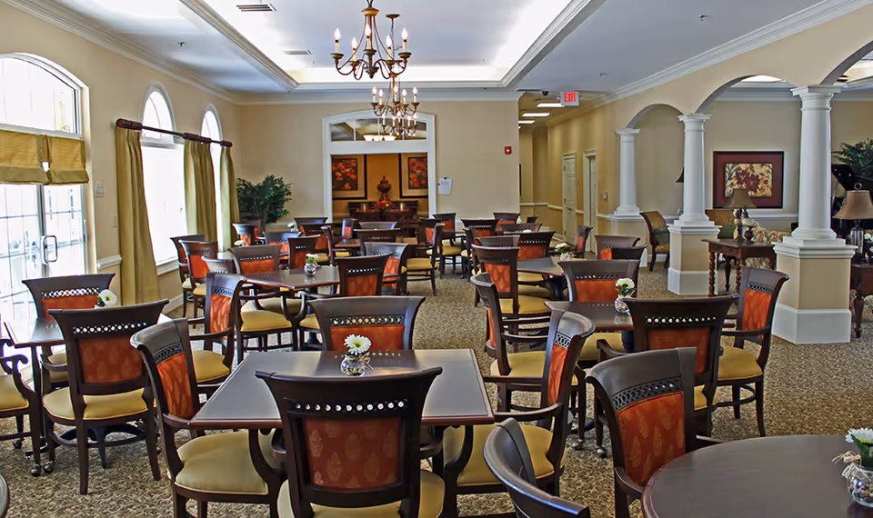 Well-lit dining room with multiple tables and chairs, chandeliers, and decorative columns.