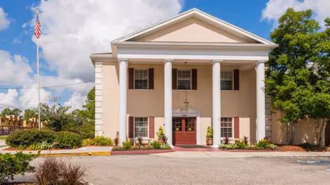 A beige neoclassical building with tall white columns, a red entry door, and an American flag.