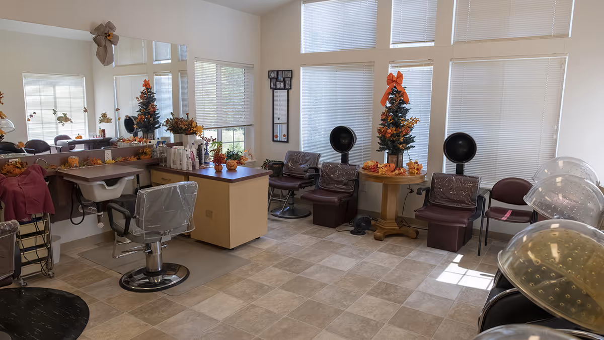 A bright salon room with styling chairs, hooded hair dryers, mirrors, and fall-themed decorations.