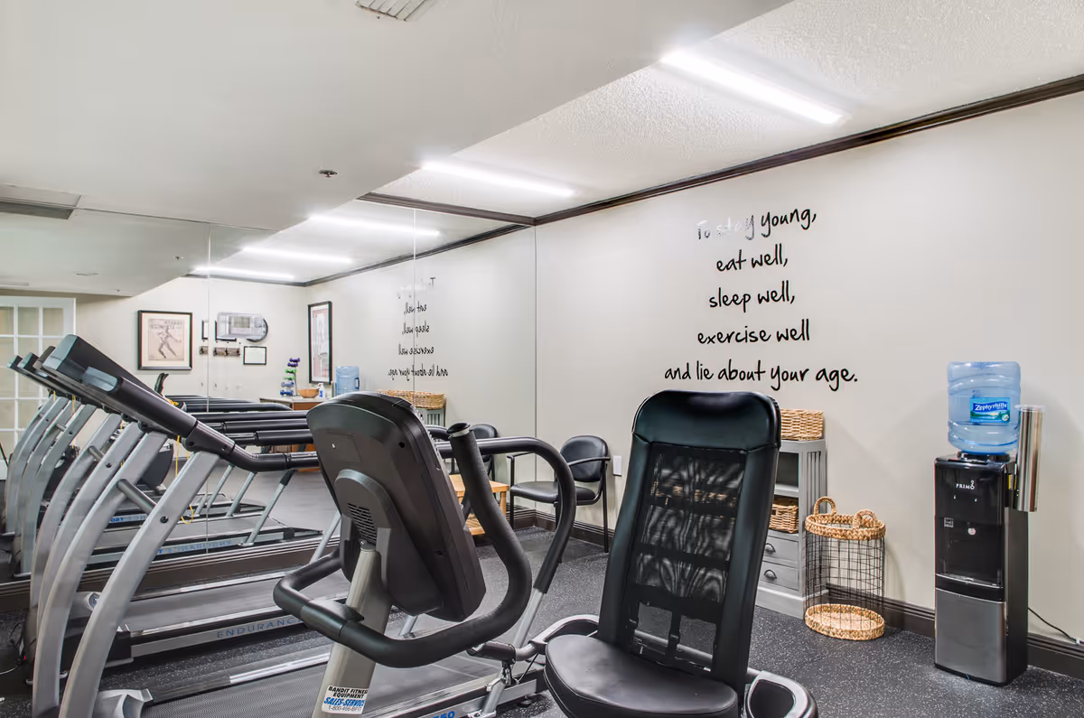 Fitness room with treadmills, a recumbent bike, mirrors, a water cooler, and a motivational wall decal.