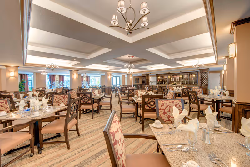 Spacious formal dining room with multiple set tables and upholstered chairs under coffered ceilings and chandeliers.
