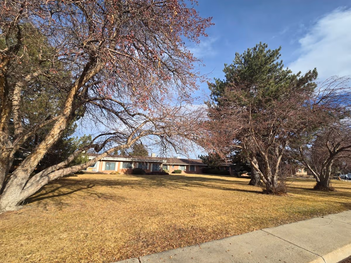 Single-story brick building set behind a grassy lawn with leafless trees under a blue sky.