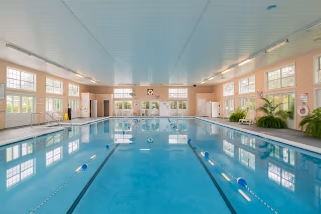 Indoor community swimming pool with lane markers in a bright room lined with large windows and seating.