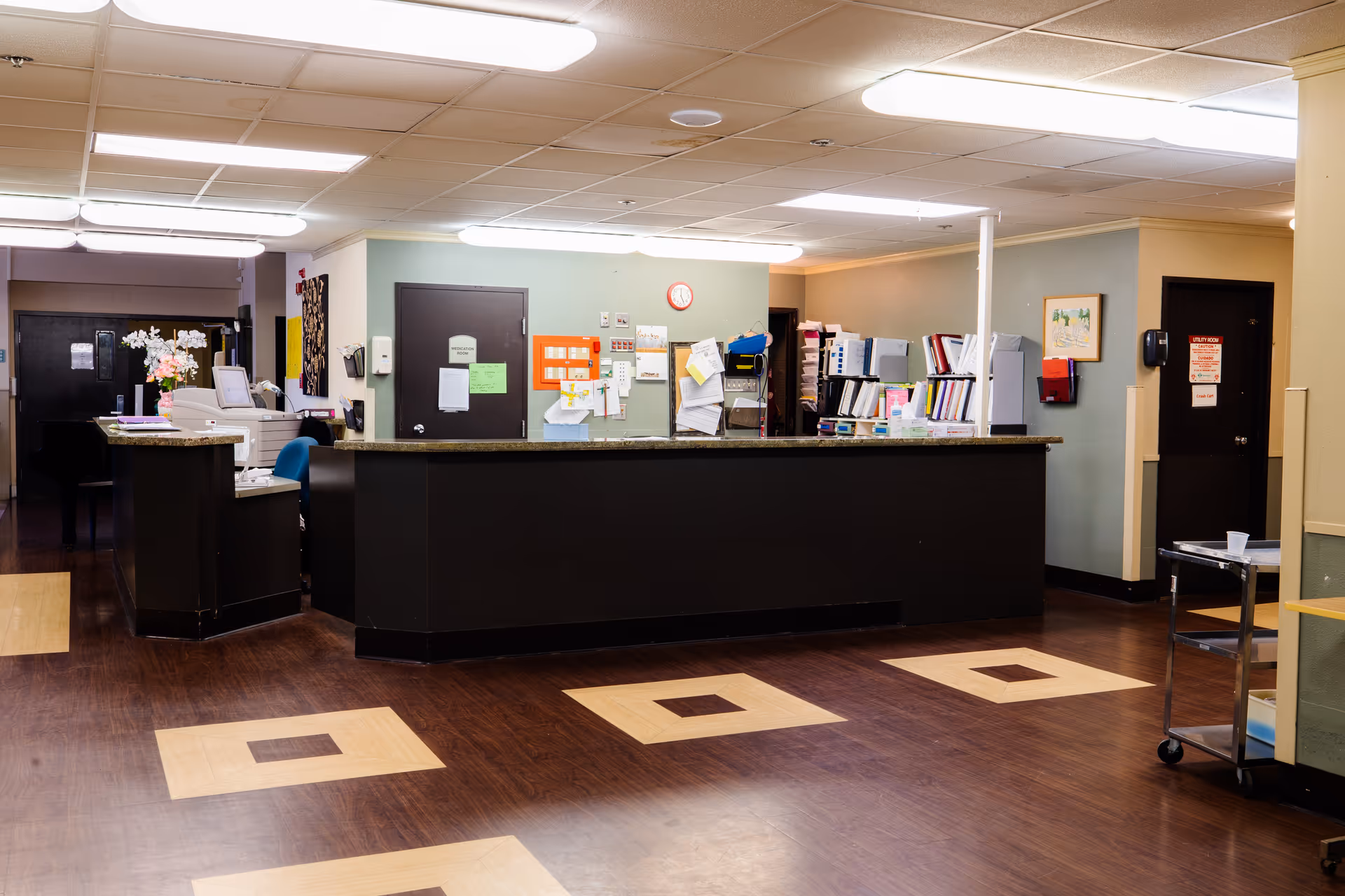 Reception and nurse station area in a senior living facility with a long front desk, paperwork, and office supplies.