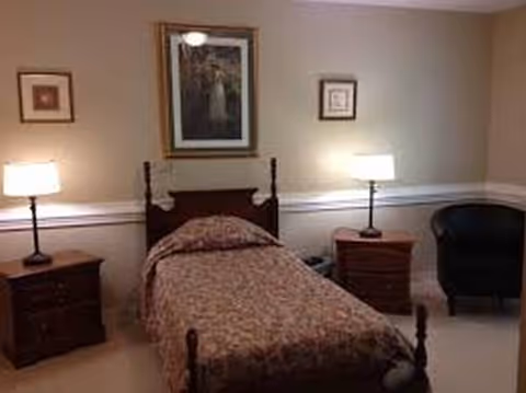 A small bedroom with a single bed, two nightstands, lamps, and a chair.
