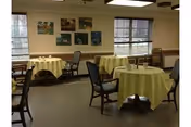 A dining room with round tables covered in yellow tablecloths and chairs.