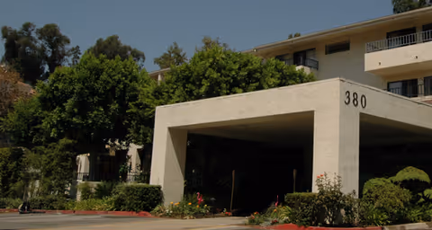 Covered entrance canopy of a multi-story residential building with the number "380" and landscaped grounds.
