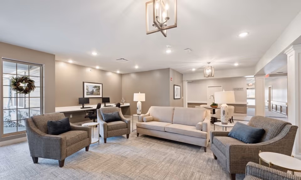 Bright furnished lobby/lounge with a sofa, four armchairs, side tables, lamps and a workstation area in the background.