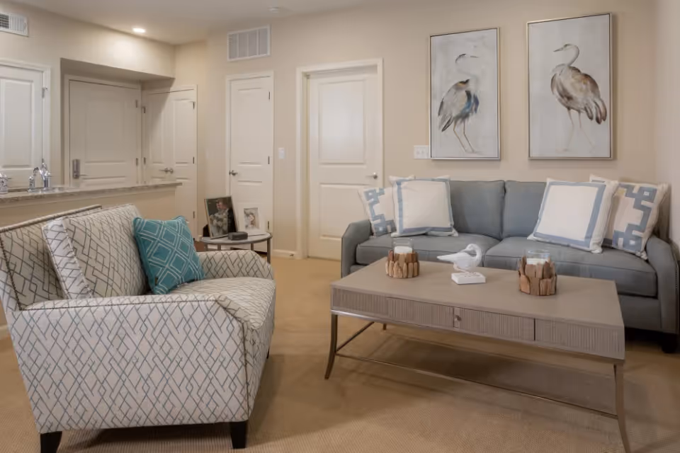 Cozy living room with a sofa, patterned armchair, coffee table, and bird artwork on the wall.