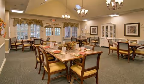 Dining room with multiple set tables and chairs, chandeliers, and a china cabinet near windows and doors.