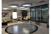 Lobby area with circular ceiling lights, a round floor pattern, seating benches and a glass water wall.