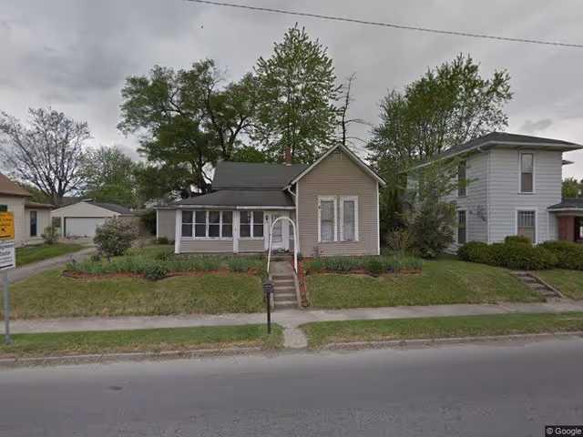 Small single-story house with an enclosed front porch, steps, and a lawn on a residential street.