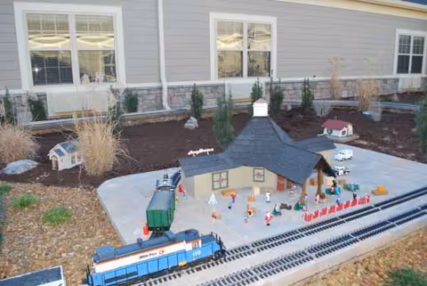 Outdoor model train layout with miniature figures and buildings beside the facility.