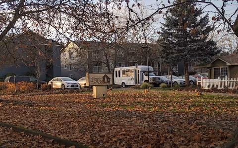 Exterior view of Conifer House facility with a parked bus and trees.