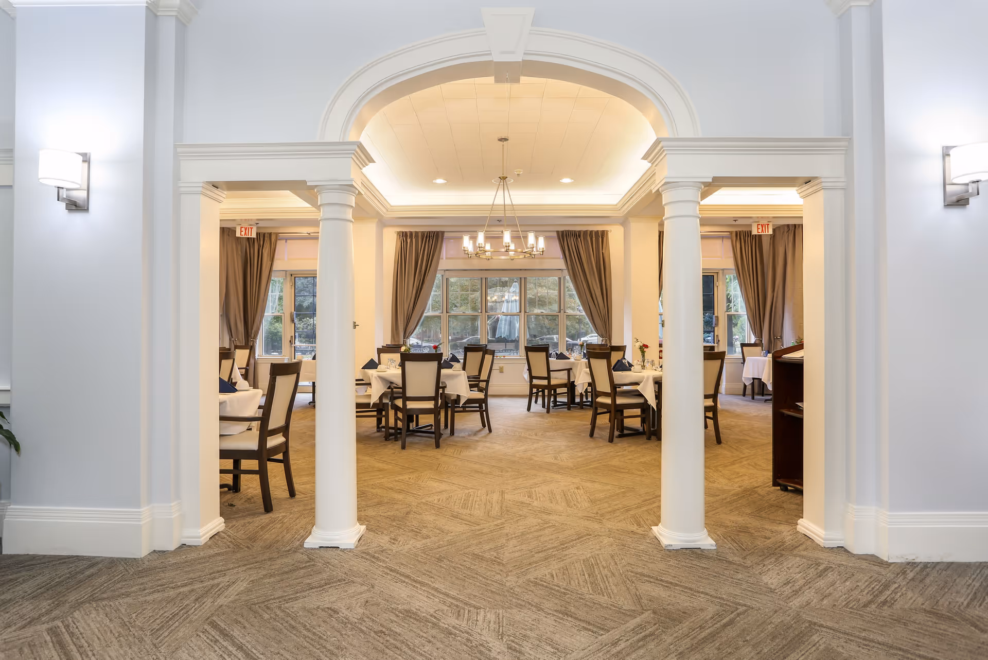 Bright elegant dining room with tables and chairs seen through decorative columns and an archway.