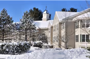 Exterior view of Summercrest Senior Living Community building covered in snow with snow-covered trees and bushes in the foreground under a clear blue sky.