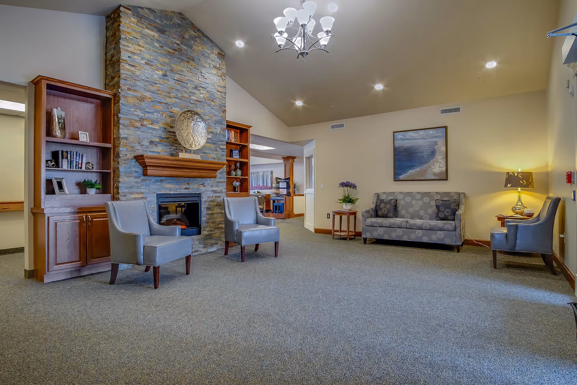 Spacious seating area in a senior living facility with armchairs and a sofa arranged around a stone fireplace and built-in shelving.