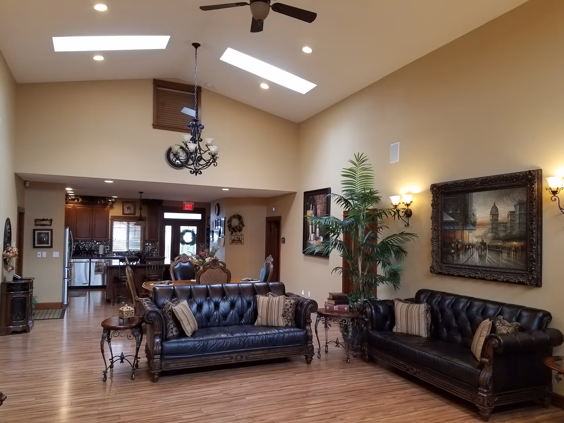 Spacious communal living room with tufted leather sofas, skylights, a chandelier, large wall art and an open view into a kitchen area.