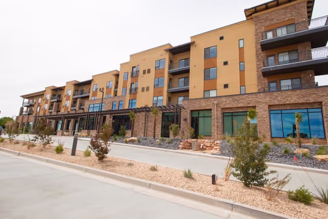 Exterior view of a multi-story building with balconies, stone facade, and landscaped driveway.