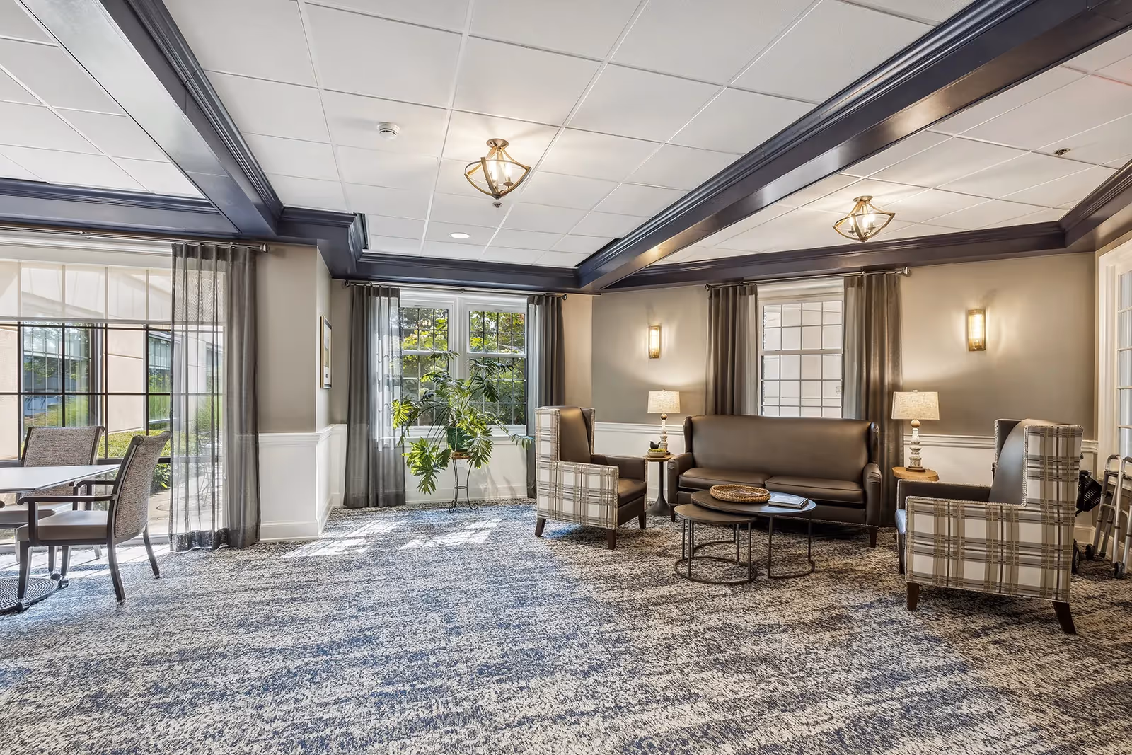 Bright communal lounge with sofas, armchairs, coffee tables, and large windows with drapes.