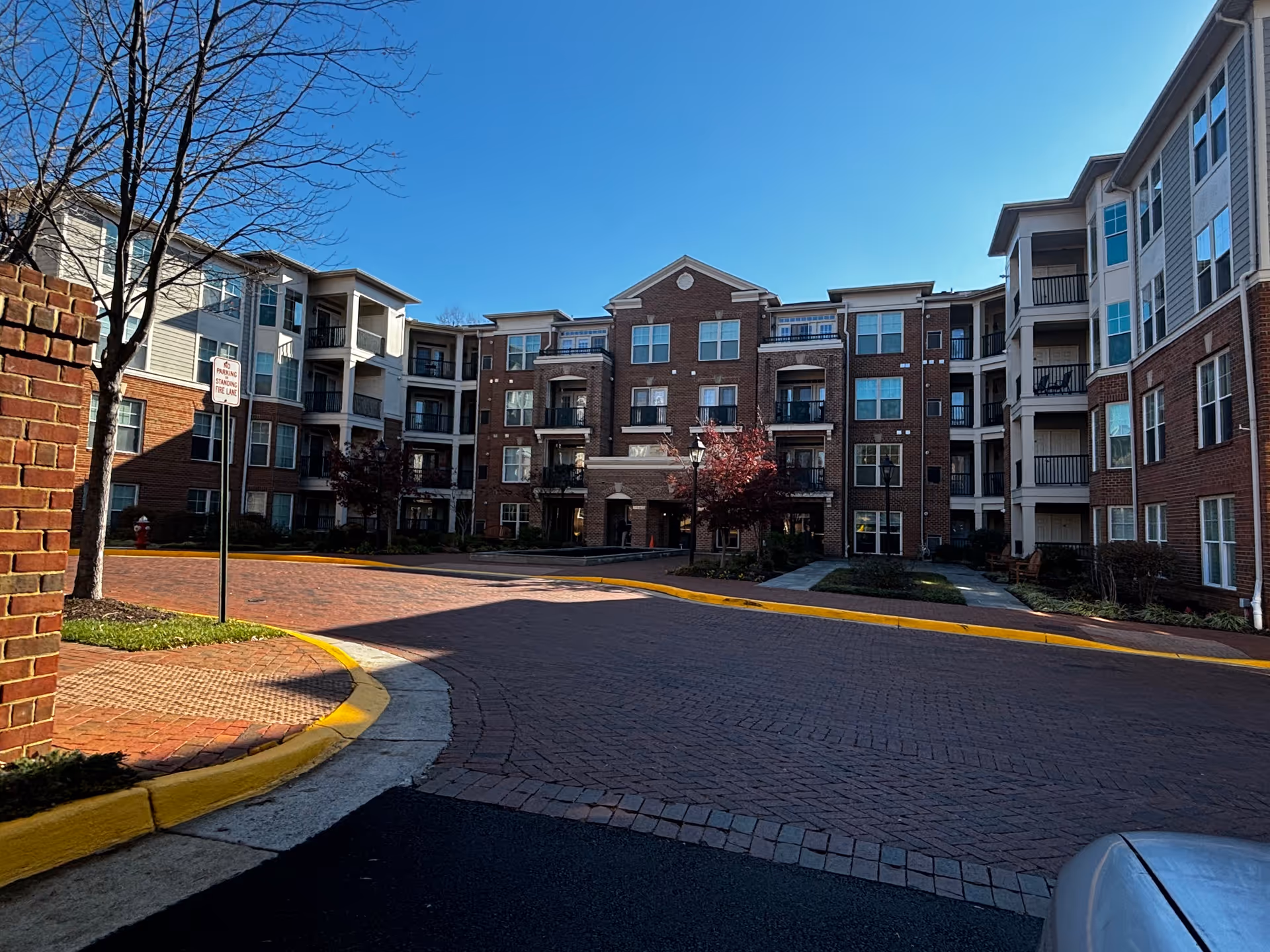 Brick-faced four-story residential building with balconies facing a circular brick driveway under a clear blue sky.