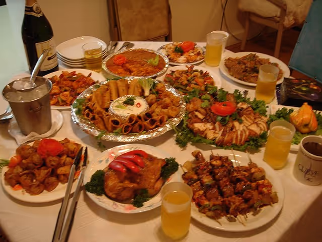 A dining table covered with many plated and foil-wrapped dishes, skewers, salads and glasses of drink.