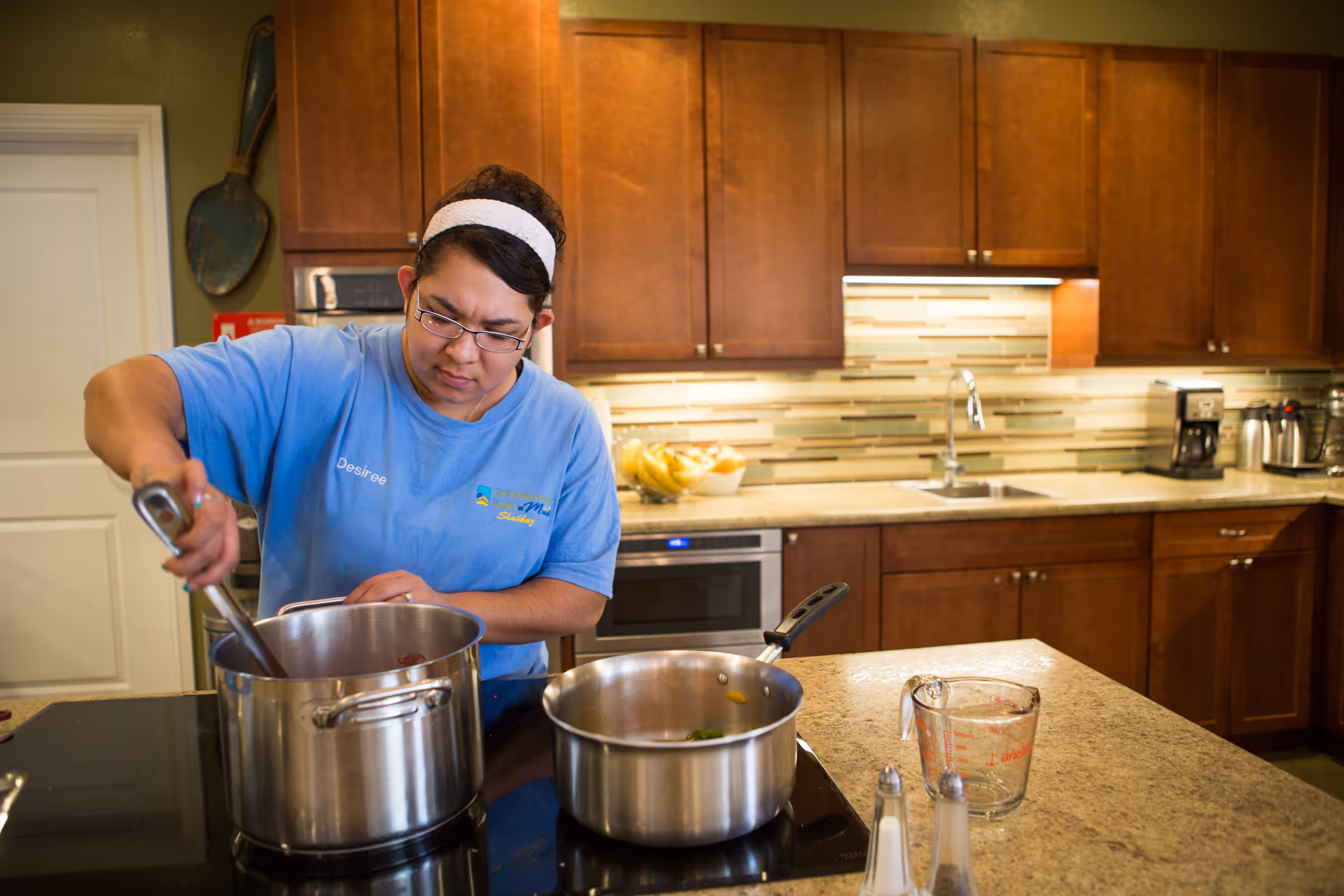 A person stirring a pot on a stovetop in a residential-style kitchen with wooden cabinets.