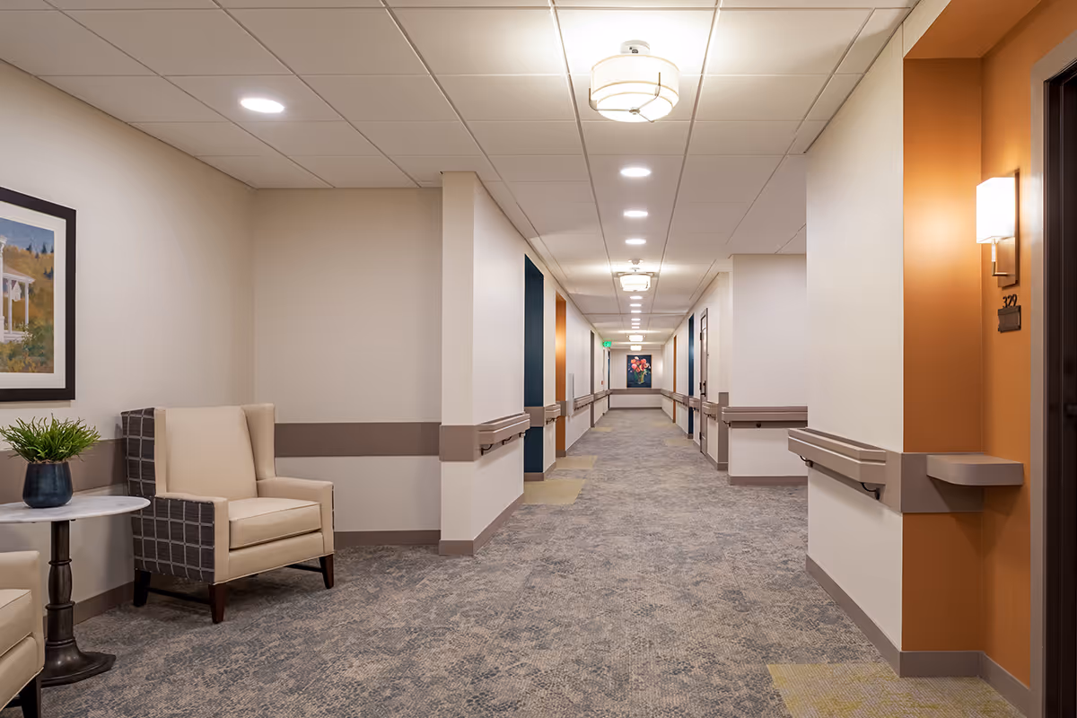 Carpeted interior hallway with seating, wall handrails, doors, and overhead lighting.