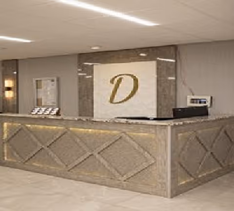 Reception desk area with a large letter 'D' displayed on the wall behind it, featuring a marble or stone finish and soft lighting.